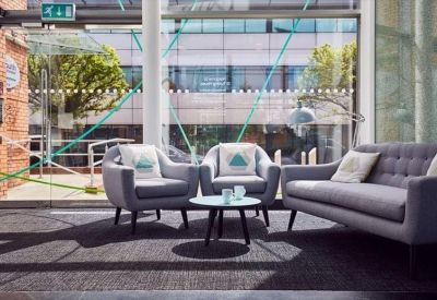 Casual breakout area with grey armchairs and a sofa near large glass windows.