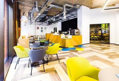 Communal cafe and coworking area with bright yellow chairs and exposed ceiling pipes.