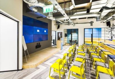 Modern presentation room with yellow chairs, a large digital screen, and industrial ceilings.