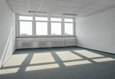 Spacious empty office with large windows and grey carpeting.