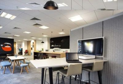 Office workstation area with high-top desks, laptops, and large wall-mounted screens.