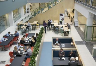 Spacious communal atrium with a cafeteria, dining tables, and a central staircase.