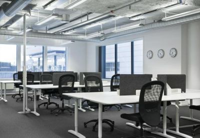 Open-plan office space with white desks, ergonomic black chairs, and exposed ceilings.