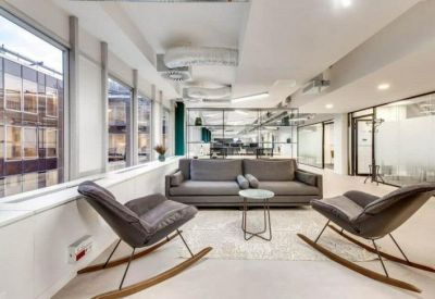 Bright breakout space with grey rocking chairs and a sofa near large windows.