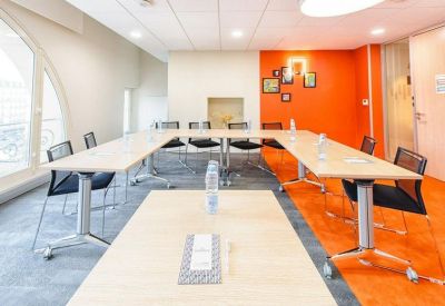 U-shaped meeting room with an orange accent wall and modern black chairs.