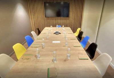 Modern meeting room with a light wood table and colorful chairs.