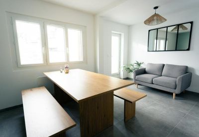 Communal dining and lounge space with a wooden table, bench seating, and grey sofa.