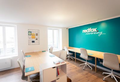 Bright coworking area with a branded teal feature wall and long shared workstations.