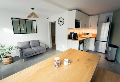 Modern kitchenette and lounge area with white cabinetry, stainless steel fridge, and small sofa.