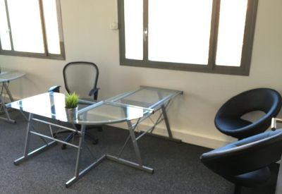 Bright private office featuring a glass L-shaped desk and black modern chairs.