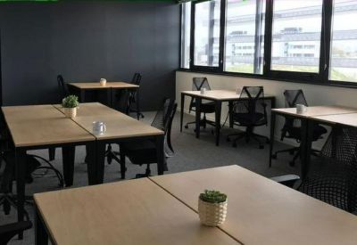 Open-plan coworking office with several light wood desks and ergonomic black mesh chairs.
