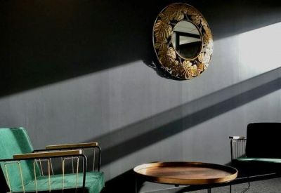 Moody lounge area with a green velvet armchair and circular wall mirror under dramatic lighting.