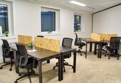 Open-plan office area with several black desks and ergonomic mesh chairs.