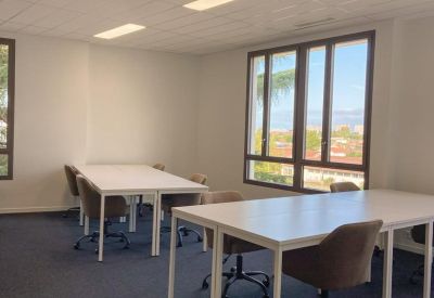 Bright workspace featuring several white desks and ergonomic chairs.