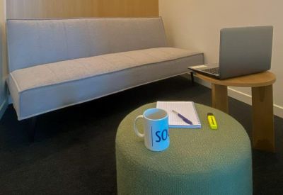 Cozy workspace featuring a grey sofa, ottoman, and green pouf.