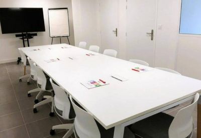 Minimalist conference room with a large white table and presentation screen.