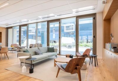 Spacious communal lounge with grey sofa, wooden accents, and large windows.