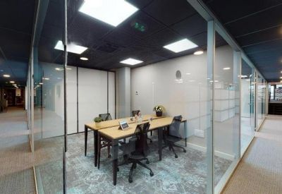 Bright glass-walled private office with shared desks and grey patterned carpet.