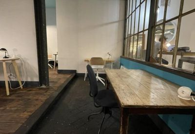 Industrial-style workspace with a private wooden desk and a view through a large interior window.