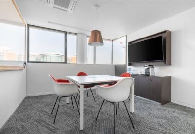 Modern four-person meeting room with a wall-mounted screen and stylish white and red chairs.
