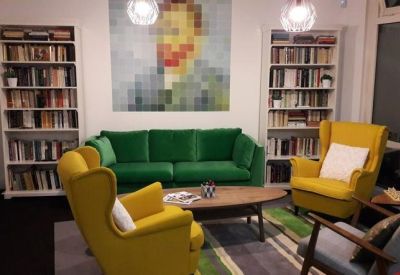 Colorful lounge area with a green velvet sofa, yellow wingback chairs, and floor-to-ceiling bookshelves.