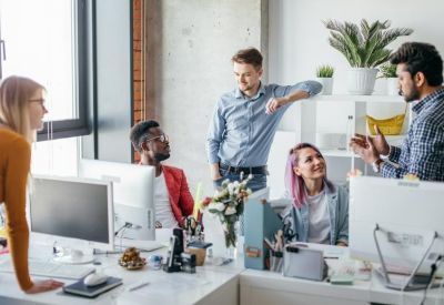 Modern open-plan office with diverse team members collaborating around white desks with plants.