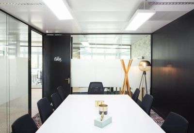 Bright conference room featuring a large white table, black chairs, and sleek glass partitions.