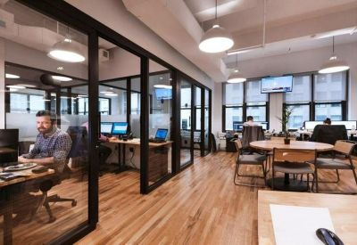 Glass-partitioned private offices and meeting rooms with wooden flooring and warm overhead lighting.