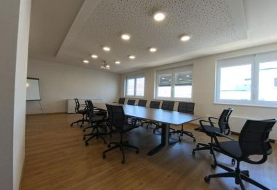 Spacious boardroom with a long wooden table, black mesh chairs, and large windows.
