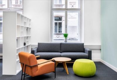 Breakout area with a dark grey sofa, wooden coffee table, orange armchair, and lime green ottoman.