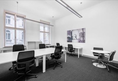 Bright shared workspace featuring long white desks and black mesh office chairs.