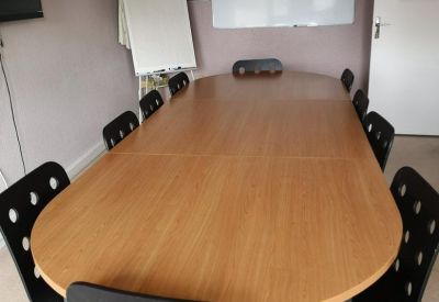 Spacious meeting room with a large wooden table, black chairs, and a whiteboard.