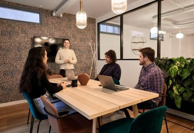 Contemporary meeting room with a light wood table, stylish green velvet chairs, and a patterned feature wall.