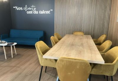 Bright communal lounge and meeting area with yellow velvet chairs, wooden table, and blue sofa.