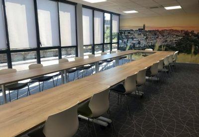 Large conference room with long wooden tables, grey chairs, and a city mural wall.