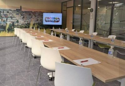 Modern meeting room setup with rows of white chairs and a digital presentation screen.