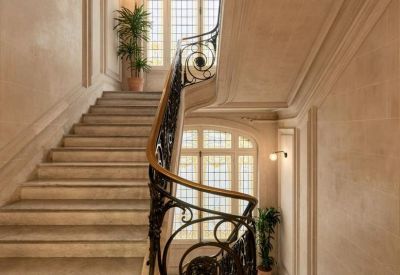 Grand stone staircase with a decorative wrought iron railing and large windows.