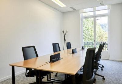 Bright meeting room with a wooden table, black ergonomic chairs, and a balcony view.