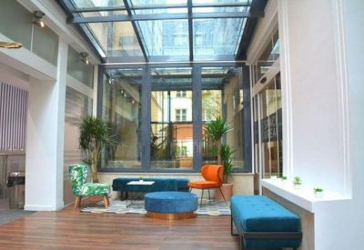 Bright glass-enclosed lounge area with a skylight, colorful velvet seating, and indoor plants.