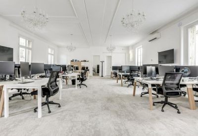 Spacious open-plan workspace with white desks, ergonomic black chairs, and ornate ceiling details.