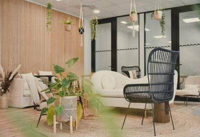 Communal lounge area with bohemian decor, white curved sofa, and hanging potted plants.