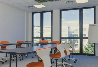 Bright training room featuring U-shaped table setup and modern white and orange chairs.