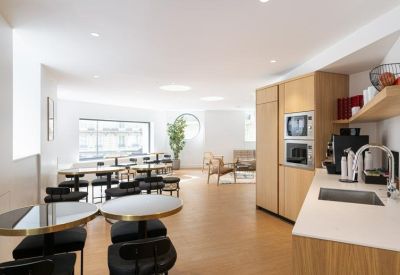 Bright cafeteria space with modern round tables and an integrated kitchenette.