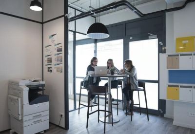 Breakout area with high stools and a printer near a large window.
