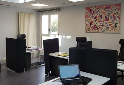 Shared office space featuring multiple workstations separated by black privacy screens and colorful wall art.