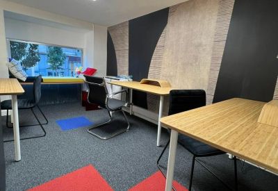 Modern workspace with multiple wooden desks, red carpet accents, and large panel lighting.