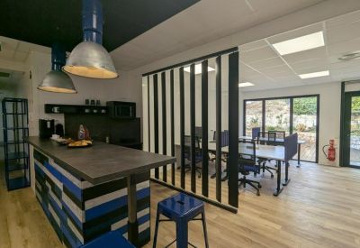 Communal break area with a kitchen island, blue bar stools, and industrial pendant lights.