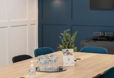 Professional boardroom with a light wood table, blue chairs, and stylish wall lighting.
