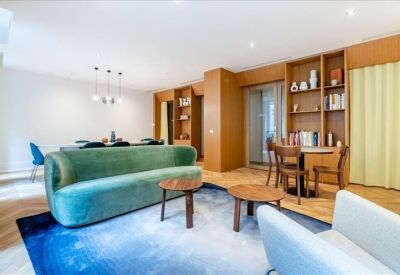 Communal lounge with a green velvet sofa, wooden bookshelves, and blue rug.