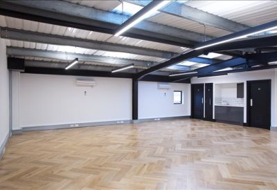Communal kitchenette area with dark cabinetry alongside an open workspace with wood floors.